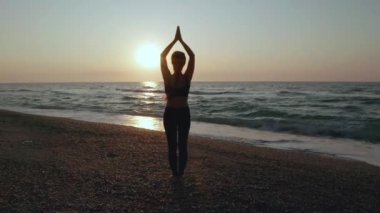 Fırtınalı denizin yakınında yoga egzersizleri yapan bir kız. Ağır çekim. Gün doğumu arkaplanı
