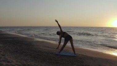 Fırtınalı denizin yakınında yoga egzersizleri yapan bir kız. Ağır çekim. Gün doğumu arkaplanı