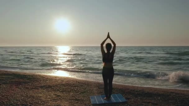 Chica haciendo ejercicios de yoga cerca del mar tormentoso. En cámara lenta. Fondo del amanecer — Vídeo de stock