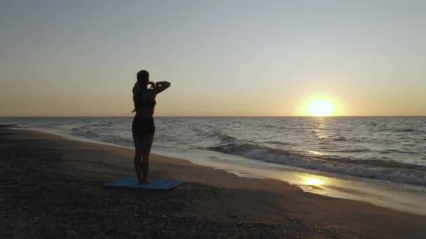 Flicka gör yogaövningar nära det stormiga havet. Sakta i backarna. Soluppgång bakgrund — Stockvideo