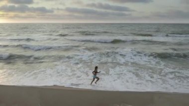 Kadın sabahın erken saatlerinde deniz kıyısında tek başına koşuyor. Gün doğumu