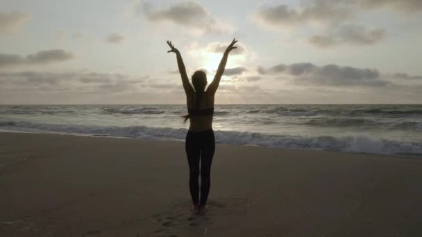 Chica haciendo ejercicios de yoga cerca del mar tormentoso. En cámara lenta. Fondo del amanecer — Vídeos de Stock