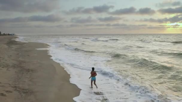 Жінка біжить сама рано вранці на морському дні. Сонячний Схід — стокове відео