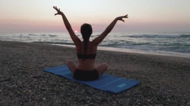 Güzel Genç Kadın Sahilde Gün Batımını izlerken Oturan Yoga Yapıyor.