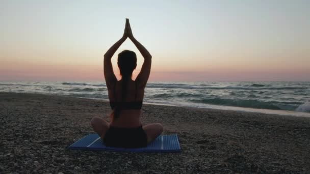 Schöne junge Frau macht sitzendes Yoga am Strand, während sie den Sonnenuntergang beobachtet. — Stockvideo