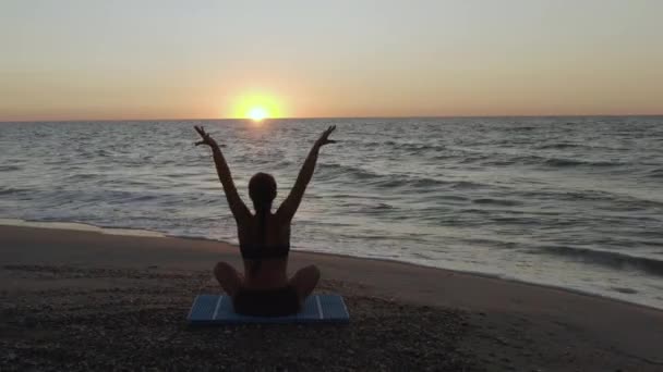 Hermosa joven haciendo yoga sentado en la playa mientras observa el atardecer . — Vídeos de Stock