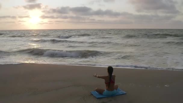 Hermosa joven haciendo yoga sentado en la playa mientras observa el atardecer . — Vídeo de stock