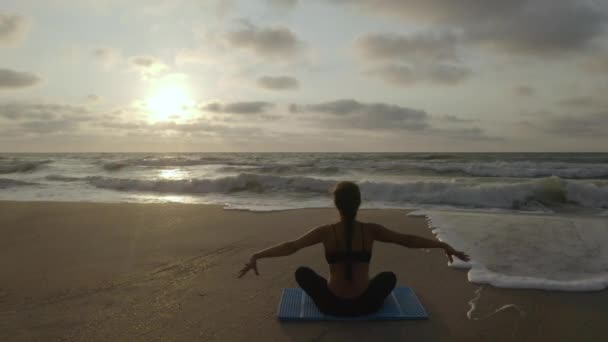 Gyönyörű fiatal nő ül jóga a strandon, miközben nézi a naplementét. — Stock videók