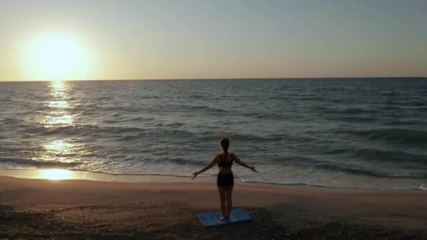 Meisje doet yoga oefeningen bij de stormachtige zee. Langzame beweging. Zonsopkomst achtergrond — Stockvideo