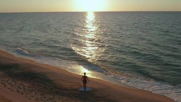 Flicka gör yogaövningar nära det stormiga havet. Sakta i backarna. Soluppgång bakgrund — Stockvideo