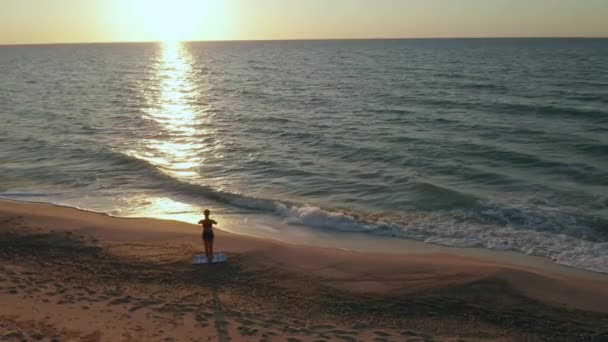 女孩在汹涌的大海边做瑜伽练习。 慢动作 日出背景 — 图库视频影像