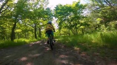 Bir çocuk ormanda bir yolda bisiklete biniyor. Bahar parkındaki yol. Çocuk sporu.