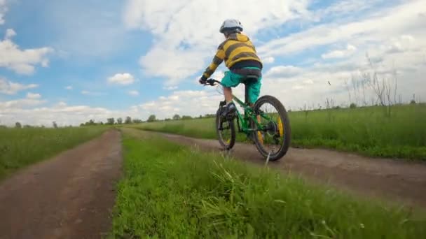 少年は畑の道を自転車に乗っている。春の公園の道路。子供スポーツ. — ストック動画