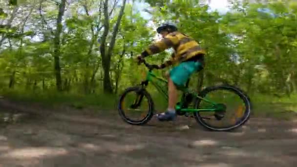 En pojke cyklar på en stig i skogen. Vägen i vårparken. Barnens idrott. — Stockvideo