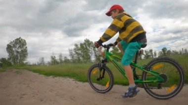 Bir çocuk nehir boyunca toprak bir yolda bisiklet sürüyor. Bulutlu hava, fırtına bulutları.