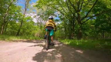 Bir çocuk ormanda bir yolda bisiklete biniyor. Bahar parkındaki yol..