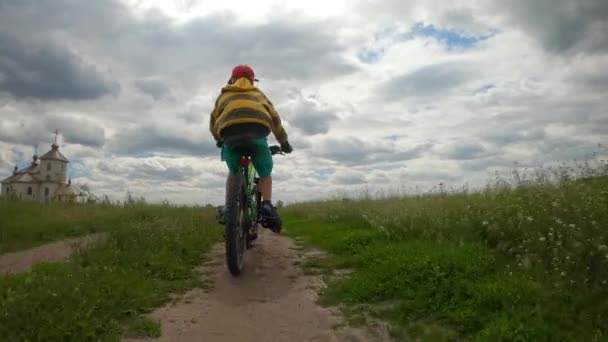 少年は川沿いの未舗装の道路を自転車で走る。曇った天気、嵐の雲. — ストック動画