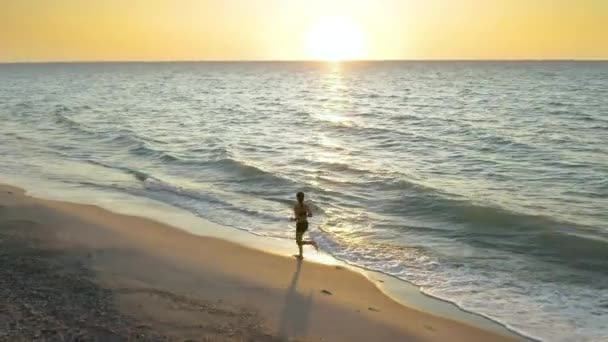 Ein schönes, junges Mädchen läuft bei Sonnenaufgang am Ozean entlang — Stockvideo