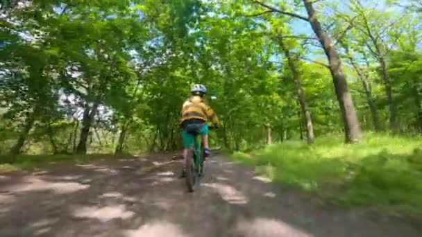 Un niño monta en bicicleta por un sendero en el bosque. El camino en el parque de primavera. — Vídeo de stock