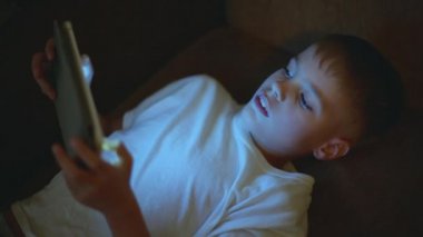 Küçük çocuk, karanlıkta oturuyor, tabletle oynuyor..