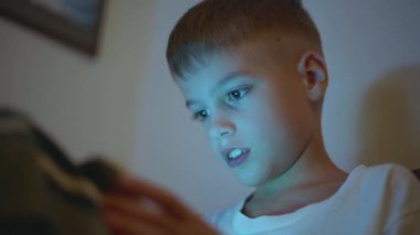 Küçük çocuk, karanlıkta oturuyor, tabletle oynuyor..