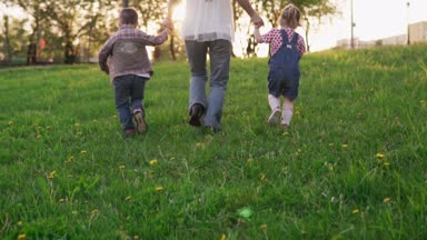 Anne ve küçük çocuklar elele ve parkta günbatımında çalışan