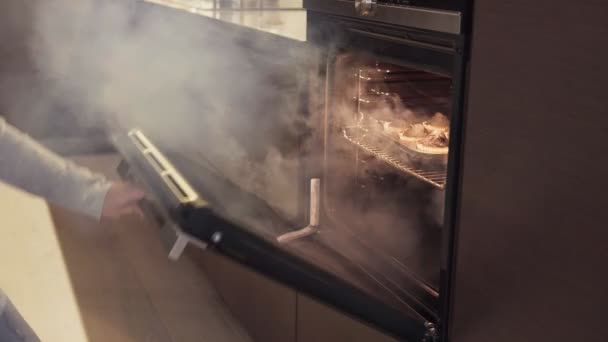 Meisje opent oven en neemt verbrande koekjes, rook van gaar voedsel komt — Stockvideo