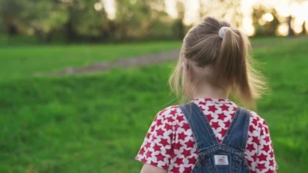 Вид ззаду на дитину, що біжить на газоні в літньому парку, повільний рух — стокове відео