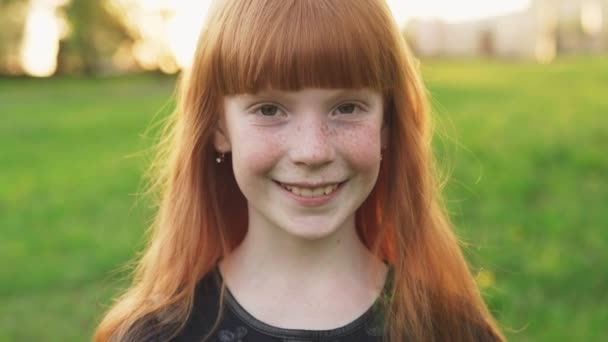 Маленькая красивая рыжая девочка с веснушками, улыбающаяся и смотрящая в камеру — стоковое видео