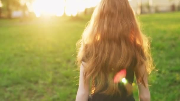 Liten vacker rödhårig flicka går för att möta solen, vänder sig om och ser in i kameran — Stockvideo