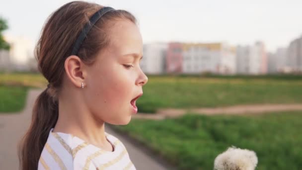 Cute little girl blowing on dandelion on city lawn in summer day, slow motion — Stock Video