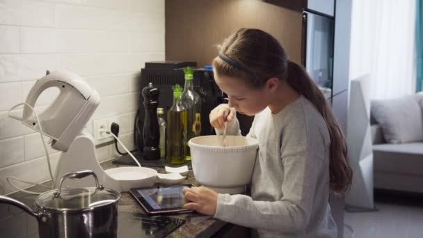 Menina aprendendo a cozinhar alimentos usando tablet na cozinha moderna — Vídeo de Stock