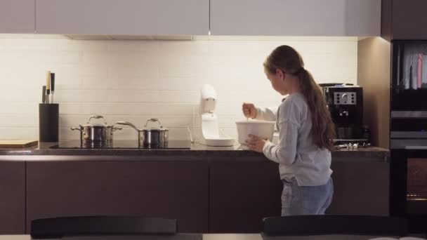 Niña está revolviendo algo en un tazón mientras se cocina en la cocina — Vídeos de Stock