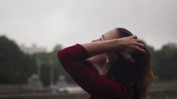 Joven mujer sensual feliz mirando a la lluvia y acariciando la cabeza con el pelo mojado — Vídeo de stock