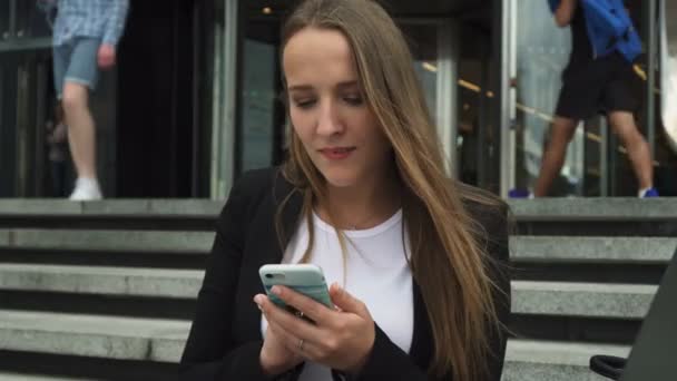 Attraktiva affärskvinna tittar på smartphone skärmen nära staden byggnad — Stockvideo