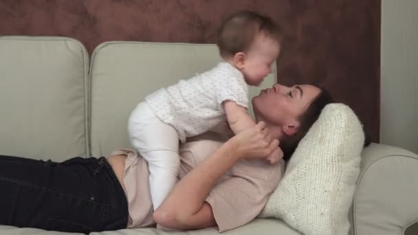 Glückliche Mutter hält ihr kleines Baby an der Hand und küsst es auf dem Sofa — Stockvideo