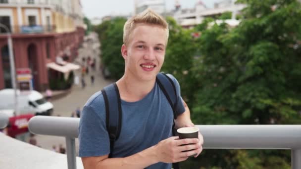 Jovem homem bonito segurando xícara de papel de café e sorrindo na cidade — Vídeo de Stock