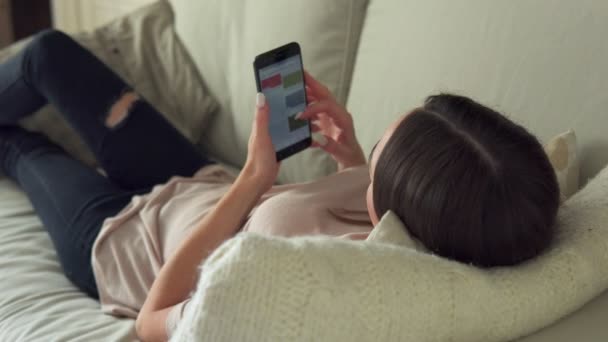 Женщина лежит дома на диване и пользуется смартфоном — стоковое видео