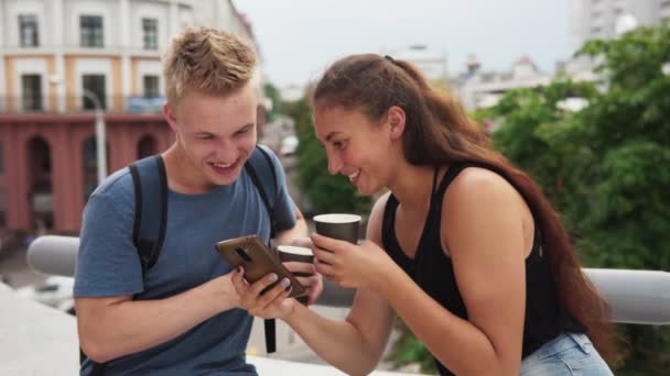 Unga lyckliga paret tittar på smartphone skärmen och skrattar åt staden gatan — Stockvideo