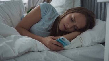 Üzgün kadın Smartphone kullanarak ve uykuya çalışıyorum yatakta yatarken