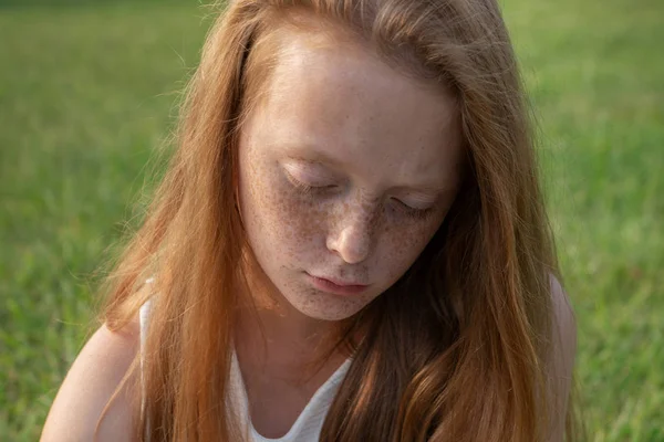 Gloomy face of sad little girl with freckles with lowered eyes Stock Picture