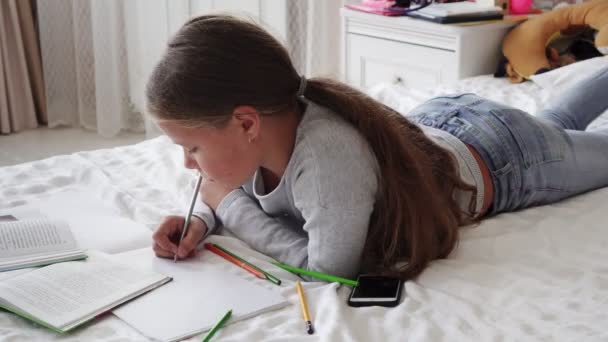 Niña de la escuela acostada en la cama y haciendo deberes — Vídeos de Stock