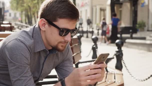 Homem de negócios em óculos de sol usa smartphone para trabalhar na manhã ensolarada na cidade — Vídeo de Stock