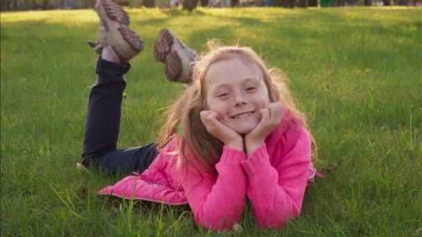 Alegre niña despreocupada acostada en la hierba y sonriendo en el parque de verano — Vídeo de stock