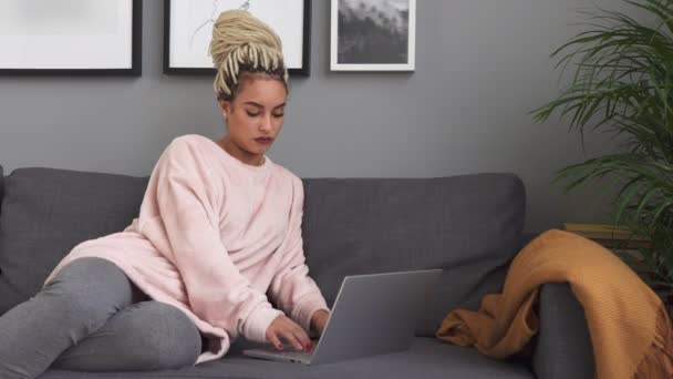 Jovem mulher usando laptop e sorrindo no sofá confortável em casa — Vídeo de Stock