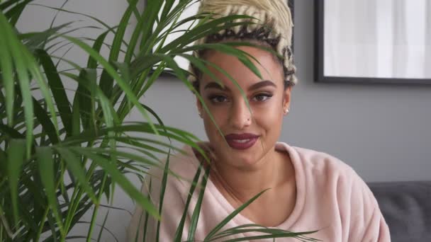 Beautiful sensual woman smiling and looking through leaves of houseplant — Stock Video