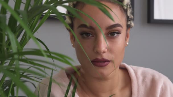 Hermosa mujer joven seria mirando a la cámara cerca de la planta de interior — Vídeos de Stock