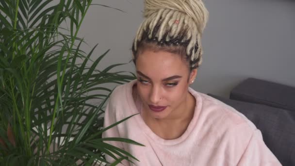 Mujer joven feliz con hermosos ojos sonriendo cerca de hojas de planta en la habitación — Vídeo de stock