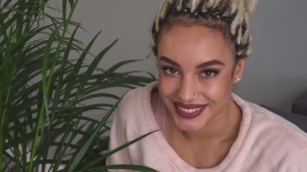 Happy girl with beautiful eyes smiling near leaves of plant in room — Stock Video