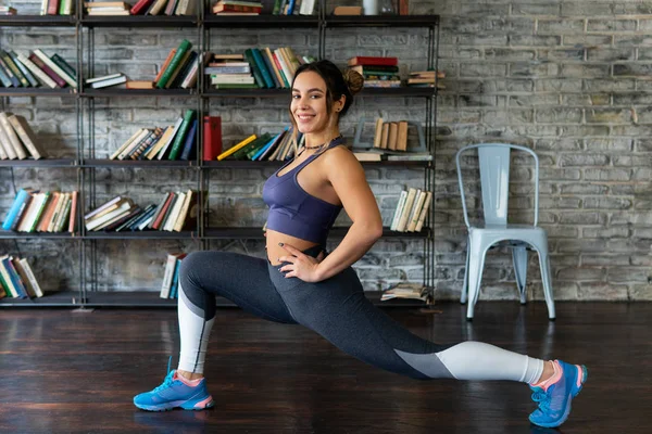 Joven mujer de fitness haciendo estiramiento de piernas y sonriendo en casa — Foto de Stock